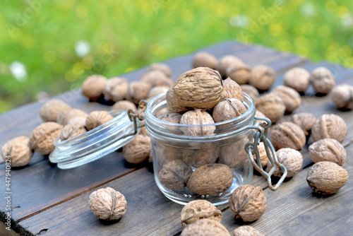 walnuts  in a glass jar and others on a wooden table and green background