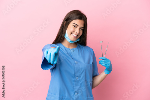 Dentist woman holding tools isolated on pink background pointing front with happy expression photo