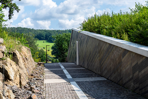 Fotografía An alley of cobblestones going between the rocks and the wall of the building in the background a field with trees