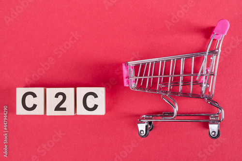 The word C2C - consumer-to-consumer, on wooden cubes, on a pink background with a shopping trolley. photo