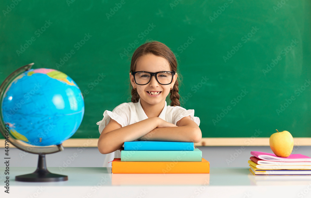 Back to school. Smart schoolgirl with glasses sitting at a lesson against the background of the school blackboard