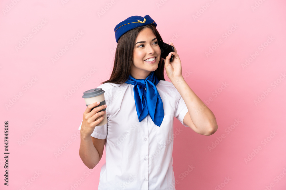 Airplane stewardess Brazilian woman isolated on pink background holding coffee to take away and a mobile Airplane stewardess Brazilian woman isolated on pink background holding coffee to take away and a mobile