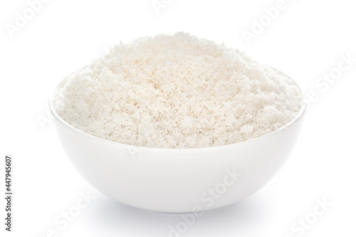 Close-up of white dry desiccated organic coconut in a white ceramic bowl over white background.