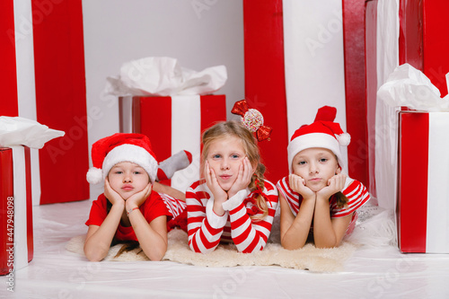 funny little girls friends in Christmas costumes against the background of big red presents.