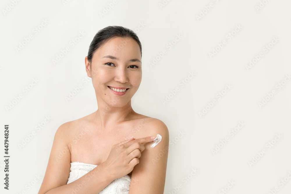a young attractive Asian woman smiles and applies a white cream on the body on a white background. the concept of body care, skin rejuvenation, preservation of youth and elasticity a young attractive Asian woman smiles and applies a white cream on the body on a white background. the concept of body care, skin rejuvenation, preservation of youth and elasticity
