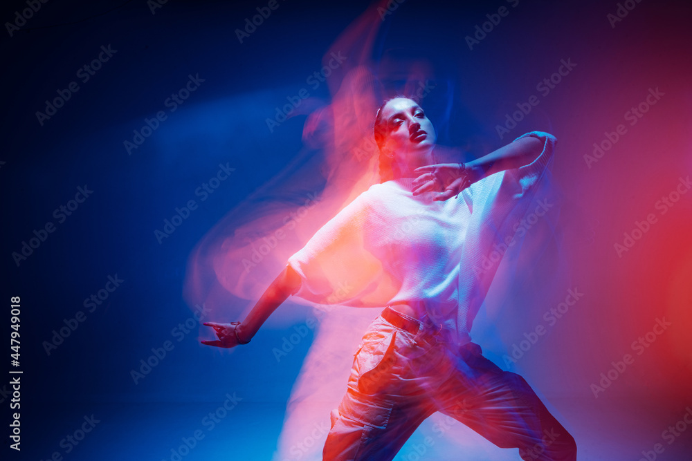 Dancing young mixed race girl enjoying moving in colorful neon studio light. Long exposure. Ethnic fiery dance