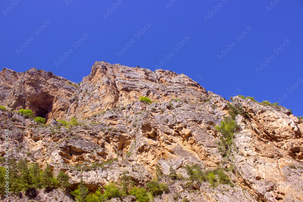 Fototapeta premium A high rock overgrown with grass against the blue sky.