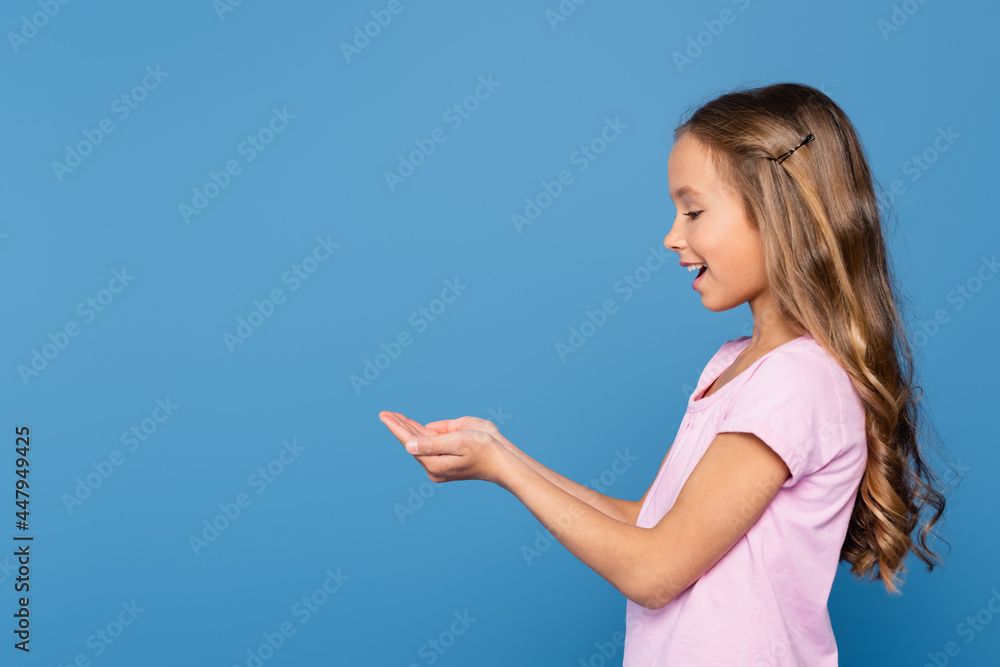 Side view of smiling girl with cupped hands isolated on blue Side view of smiling girl with cupped hands isolated on blue