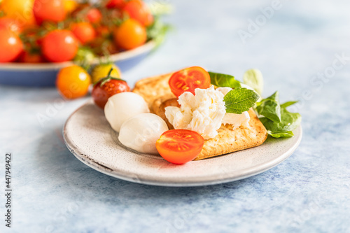 Crackers with cherry tomatoes, green salad and mozzarella, blue concrete background.