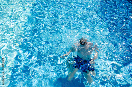 Caucasian man in swimming trunks under water dives in the pool with blue tiles on vacation. Adult male swims in swimming pool with azure water. Summer holidays concept.
