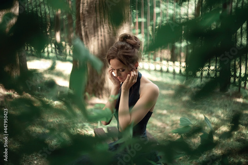 Fototapeta Naklejka Na Ścianę i Meble -  Portrait of a young sad girl with her head bowed through the leaves