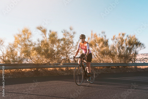 A young female cyclist riding her bike on the asphalt during sunset. Cycling concept. Sport concept.