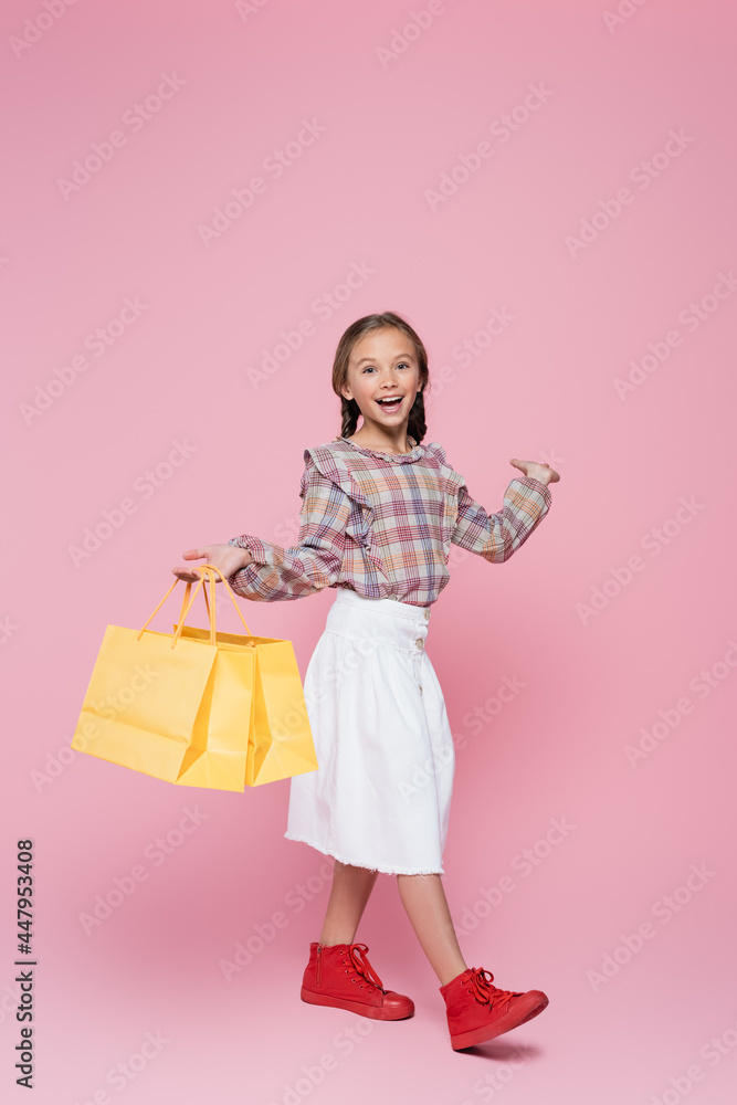 Smiling kid with shopping bags pointing at pink background Smiling kid with shopping bags pointing at pink background