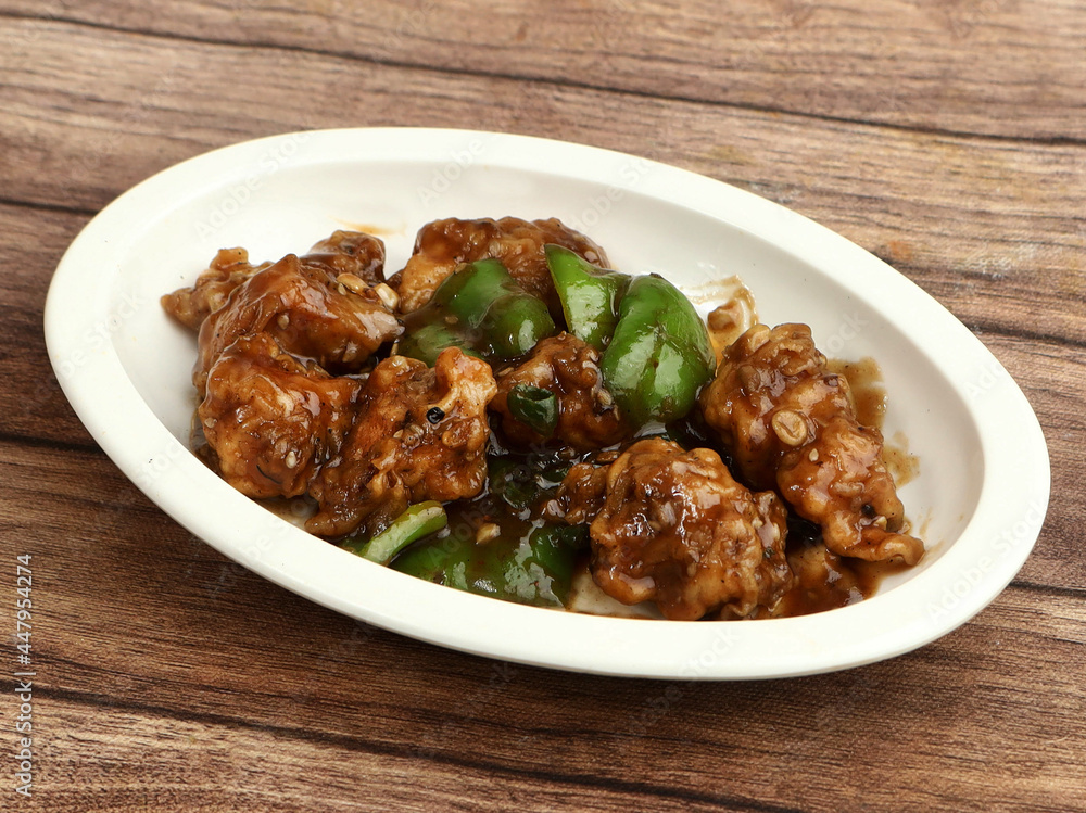 Gobi Manchurian, Popular indo-chinese food made of cauliflower florets, served in a white plate over a rustic wooden table. selective focus Gobi Manchurian, Popular indo-chinese food made of cauliflower florets, served in a white plate over a rustic wooden table. selective focus