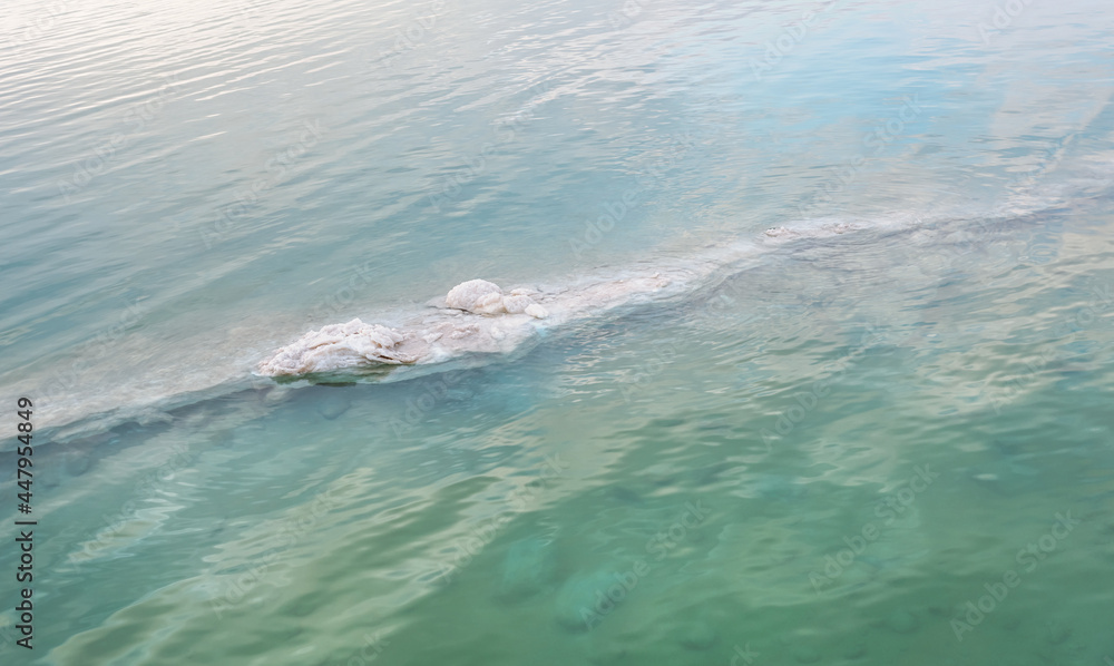 Sand covered with crystalline salt on shore of Dead Sea, clear calm water near - typical scenery at Ein Bokek beach, Israel