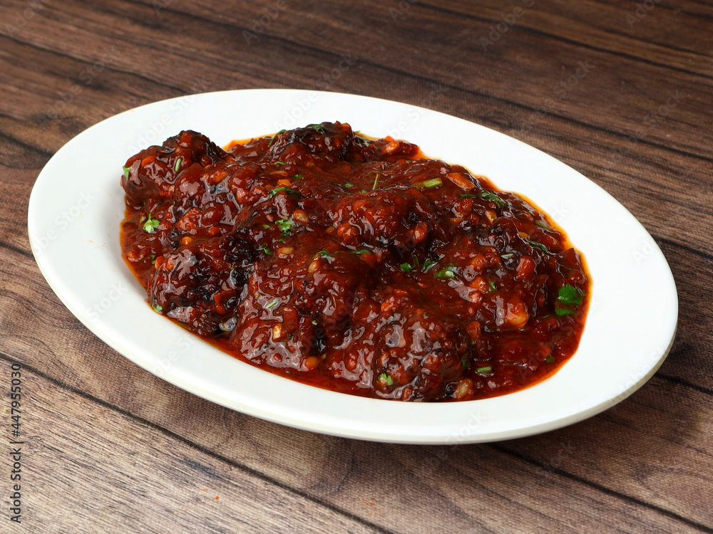 Veg Manchurian, Popular indo-chinese food made of cauliflower florets and other vegetable, served in a white plate over a rustic wooden table. selective focus Veg Manchurian, Popular indo-chinese food made of cauliflower florets and other vegetable, served in a white plate over a rustic wooden table. selective focus