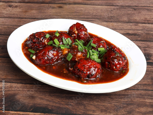 Veg Manchurian, Popular indo-chinese food made of cauliflower florets and other vegetable, served in a white plate over a rustic wooden table. selective focus photo