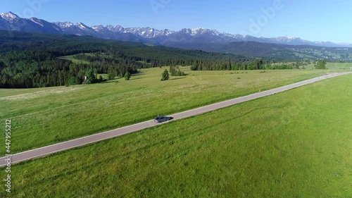 Aerial view of mountain road and luxury sedan driving on an empty road. In the background wide Tatra mountains range. Concept: Vacations in mountains, family road trip, traveling, going to holidays.