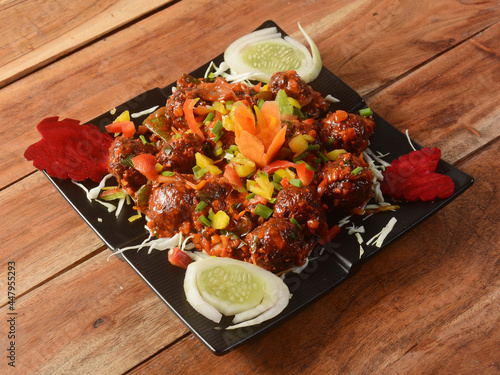 Veg Manchurian, Popular indo-chinese food made of cauliflower florets and other vegetable, served in a black plate over a rustic wooden table. selective focus photo