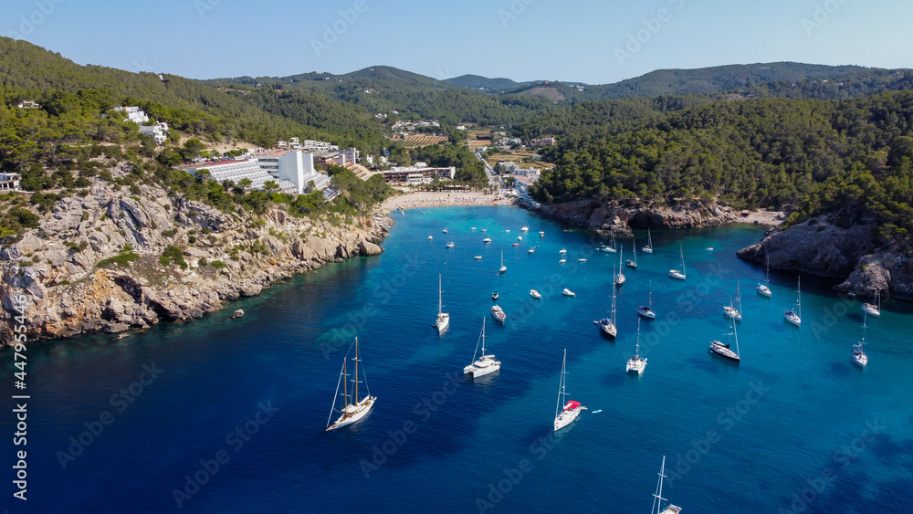 Naklejka premium Aerial view of the beach of Port Sant Miquel on the north shore of Ibiza island in Spain - Isolated bay sided with large hillside hotels in the Balearic Islands