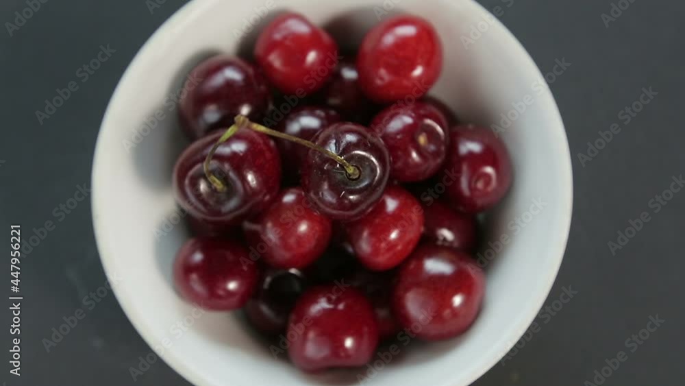 Ripe juicy cherry in a white bowl on a black background rotates in a circle top view Ripe juicy cherry in a white bowl on a black background rotates in a circle top view