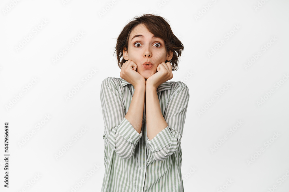 Cute and lovely girl, brunette woman pucker lips, say wow, looking with interest, intrigued by smth, watching with fascinated face, standing against white background Cute and lovely girl, brunette woman pucker lips, say wow, looking with interest, intrigued by smth, watching with fascinated face, standing against white background
