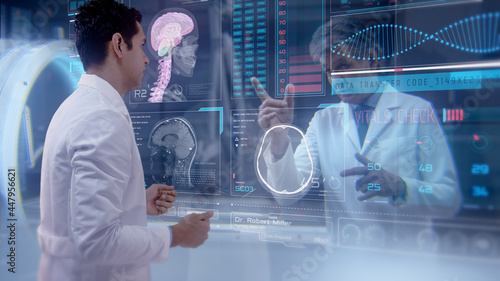 Two doctors having an online video conference analyze a patient\'s medical MRI diagnosis by checking on a large glass screen with futuristic holograms. Concept of: medicine, doctors, future, holography