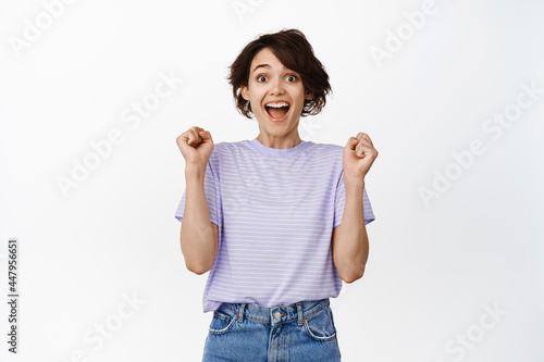 Hooray. Happy winner girl jumping excited, look surprised, winning and celebrating, triumphing, stare at prize joyful, standing against white background