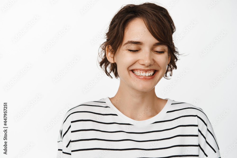 Close up portrait of attractive happy woman, smiling with closed eyes, romantic natural girl with glowing clean facial skin, standing against white background Close up portrait of attractive happy woman, smiling with closed eyes, romantic natural girl with glowing clean facial skin, standing against white background