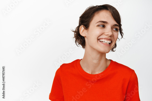 Close up portrait of carefree brunette girl laughing, smiling happy, looking aside, standing over white background © Cookie Studio