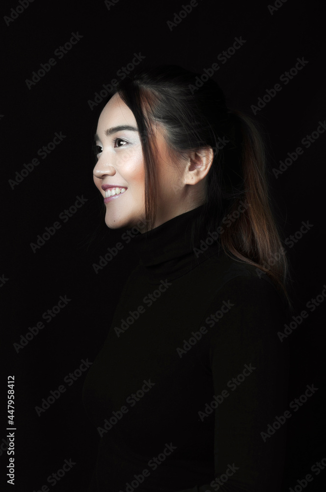 Smiling young asian woman, profile portrait with black shirt on black background. Vertical version