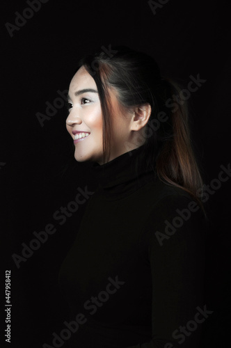 Smiling young asian woman, profile portrait with black shirt on black background. Vertical version