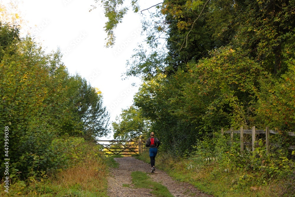 Jogger running along a gravel dirt path on a sunny early autumn morning Riddlesdown Surrey England October 2020