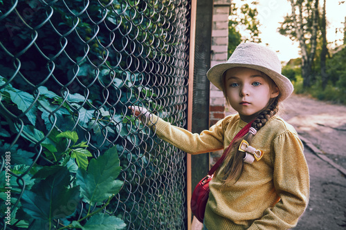 A girl in a yellow jacket with a lurex and a gray hat stands at the net of a rabitsa and looks thoughtfully. A girl with a pink handbag over her shoulder photo