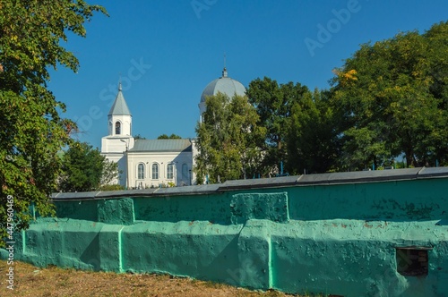 White-stone two-domed church above ancient fence under green tree photo