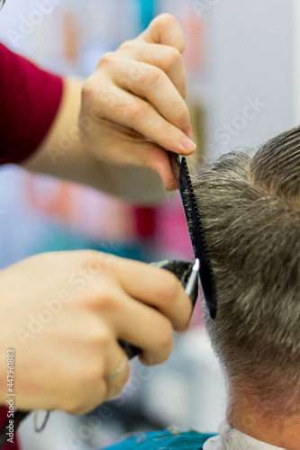 The hairdresser cuts the man's hair with a clipper and comb. Short men's haircut.