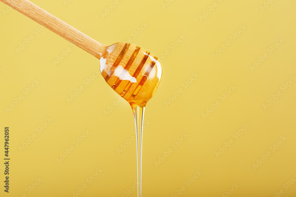 Golden honey trickles from a wooden honey dipper on a yellow background Golden honey trickles from a wooden honey dipper on a yellow background