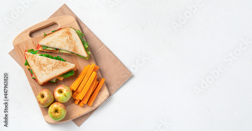 Sandwiches, apples and carrots on a board on a kraft bag on a gray background. Preparing a school lunch. Top view, copy space.