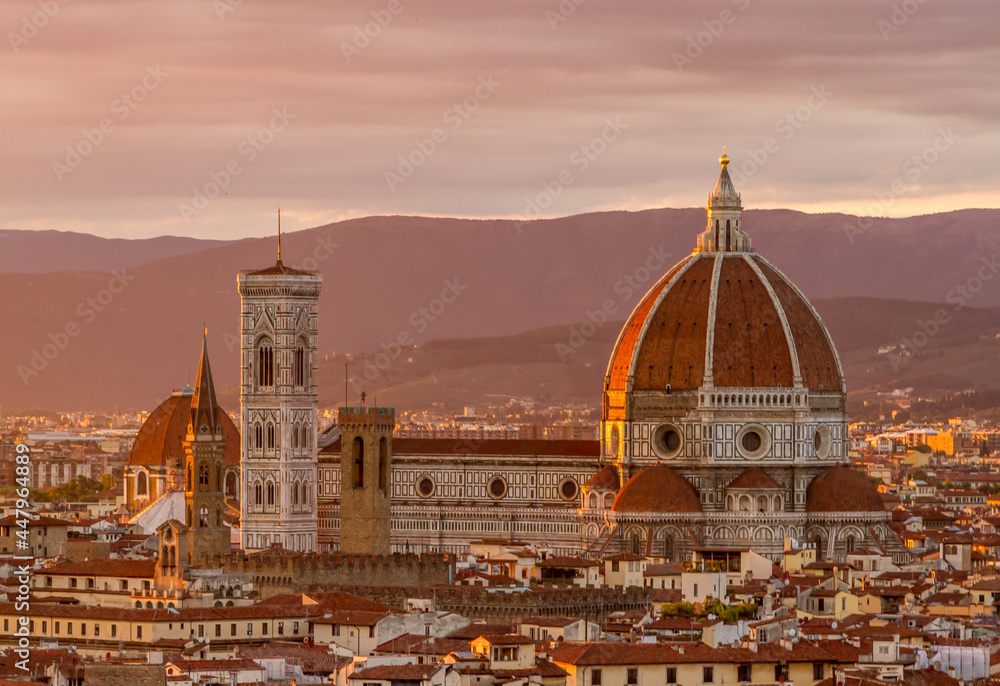 Florence's beautiful Gothic cathedral standing out over the surrounding city buildings, with the mountains in the background at sunset