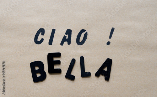the expression "ciao!" stencilled in black paint on craft paper background with holes - and the word bella in black chalk letters
