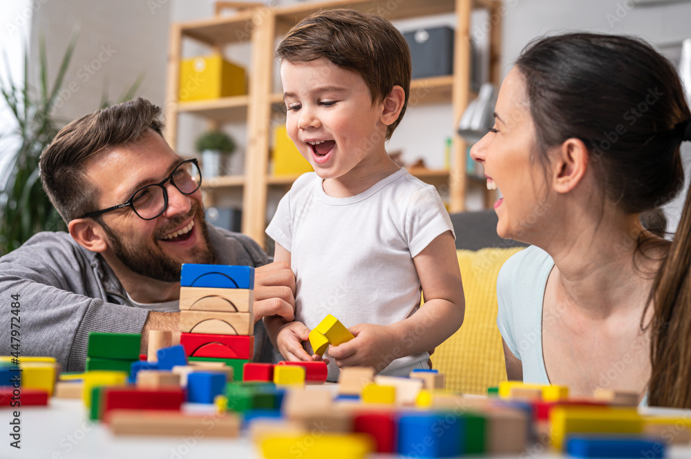 Fototapeta premium Young happy family. Mother and father playing with her cute toddler son at home using didactic wooden toys. Home education