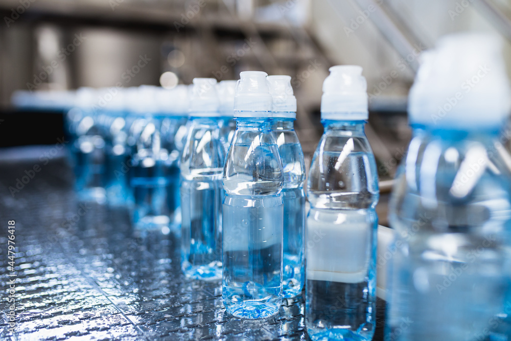Bottling plant - Water bottling line for processing and bottling pure spring water into blue bottles. Selective focus. Bottling plant - Water bottling line for processing and bottling pure spring water into blue bottles. Selective focus.