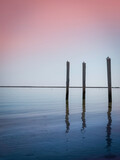 Seascape with three pilings. Abstract minimalist image of the horizon and vertical poles. Pink sunset and blue sea water reflections in Hyannis Harbor beach in Massachusetts.