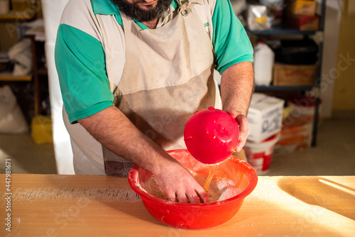 Cocinero masando harina en la mesa para luego cortar la masa con un cuchillo y preparar los bizcochos. photo