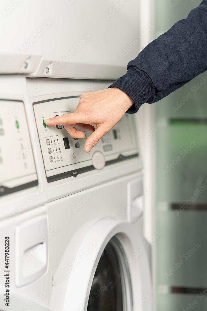 Close-up view of a hand about to press the green start button of the washing machine Close-up view of a hand about to press the green start button of the washing machine