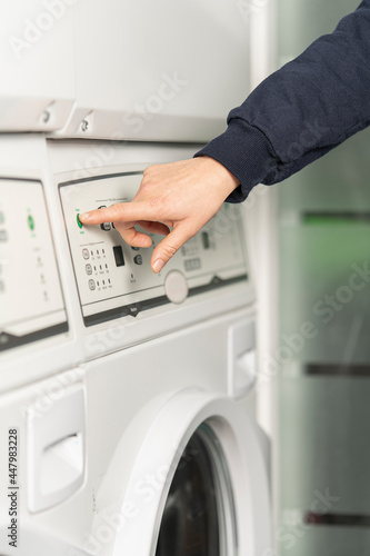 Close-up view of a hand about to press the green start button of the washing machine