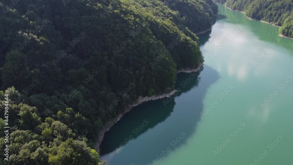 Aerial tilt up shot of the beautiful forest hitting the calm lake Paltinu of Doftana Valley in Romania in the early afternoon Aerial tilt up shot of the beautiful forest hitting the calm lake Paltinu of Doftana Valley in Romania in the early afternoon