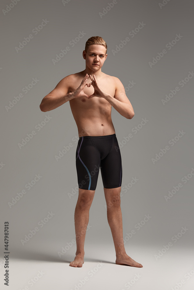 Athlete swimmer on a gray background stands and shows his folded heart with his hands, gray background.