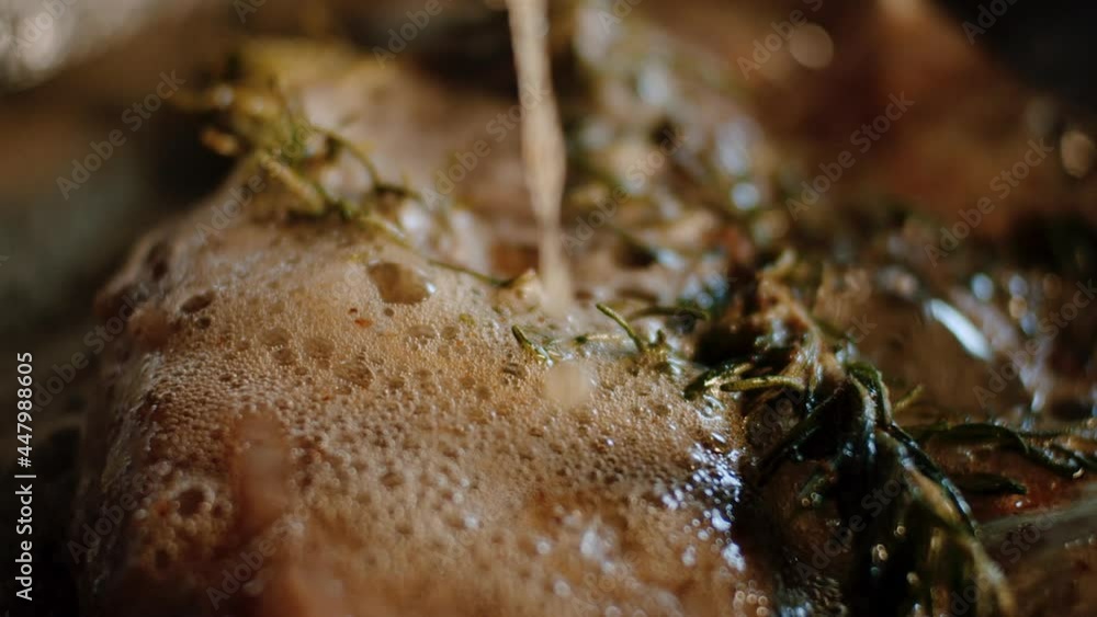 Spoon melted butter over meat in pan with rosemary, close up Spoon melted butter over meat in pan with rosemary, close up