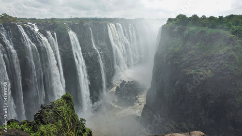 The streams of Victoria Falls rush into the abyss. At the bottom of the gorge flows a stormy river with a rocky bed. Zimbabwe